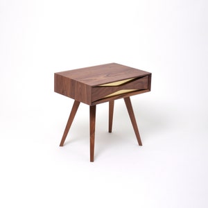 May include: A dark wood nightstand with a single drawer featuring a gold metal accent. The drawer is open and the nightstand has a simple, modern design.
