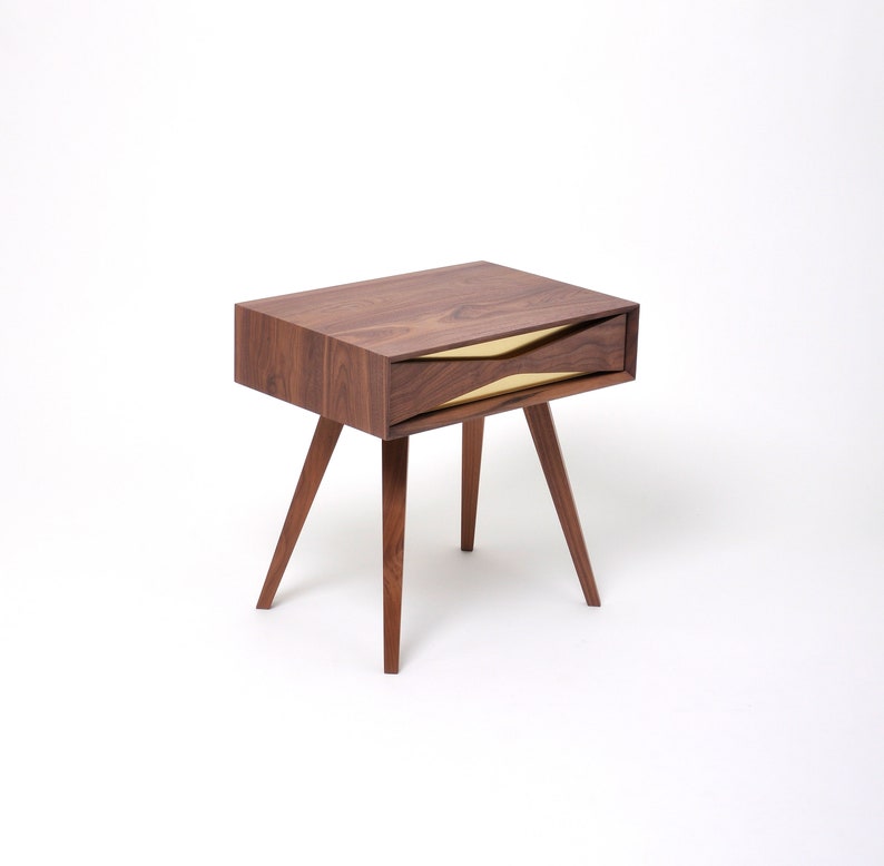 May include: A dark wood nightstand with a single drawer featuring a gold metal accent. The drawer is open and the nightstand has a simple, modern design.
