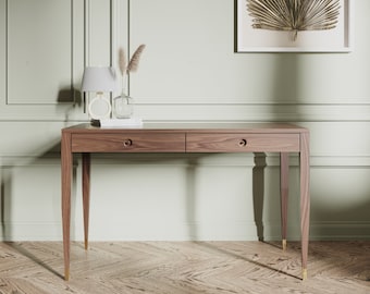 May include: A wooden desk with two drawers and tapered legs. The desk has brass hardware and sits on a wood floor.