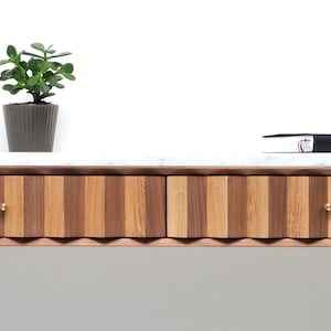 May include: A walnut and oak wood console table with two drawers and a white marble top. The table has a wavy, scalloped edge and brass drawer pulls. A small potted plant sits on the table.