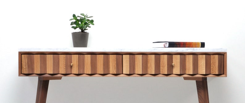 May include: A walnut and oak wood console table with two drawers and a white marble top. The table has a wavy, scalloped edge and brass drawer pulls. A small potted plant sits on the table.