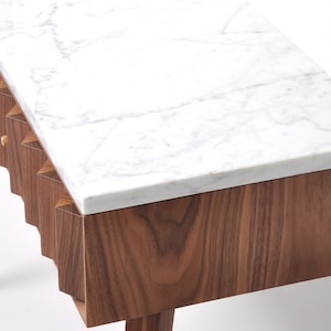 May include: A table with a white marble top and a walnut wood base. The base has a distinctive, geometric design with a series of vertical, angled panels.