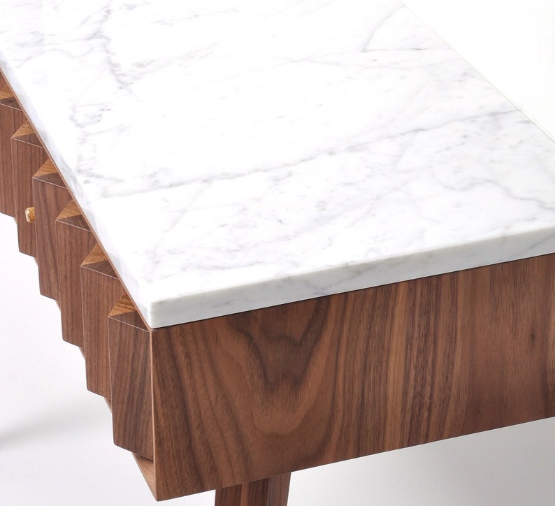 May include: A table with a white marble top and a walnut wood base. The base has a distinctive, geometric design with a series of vertical, angled panels.