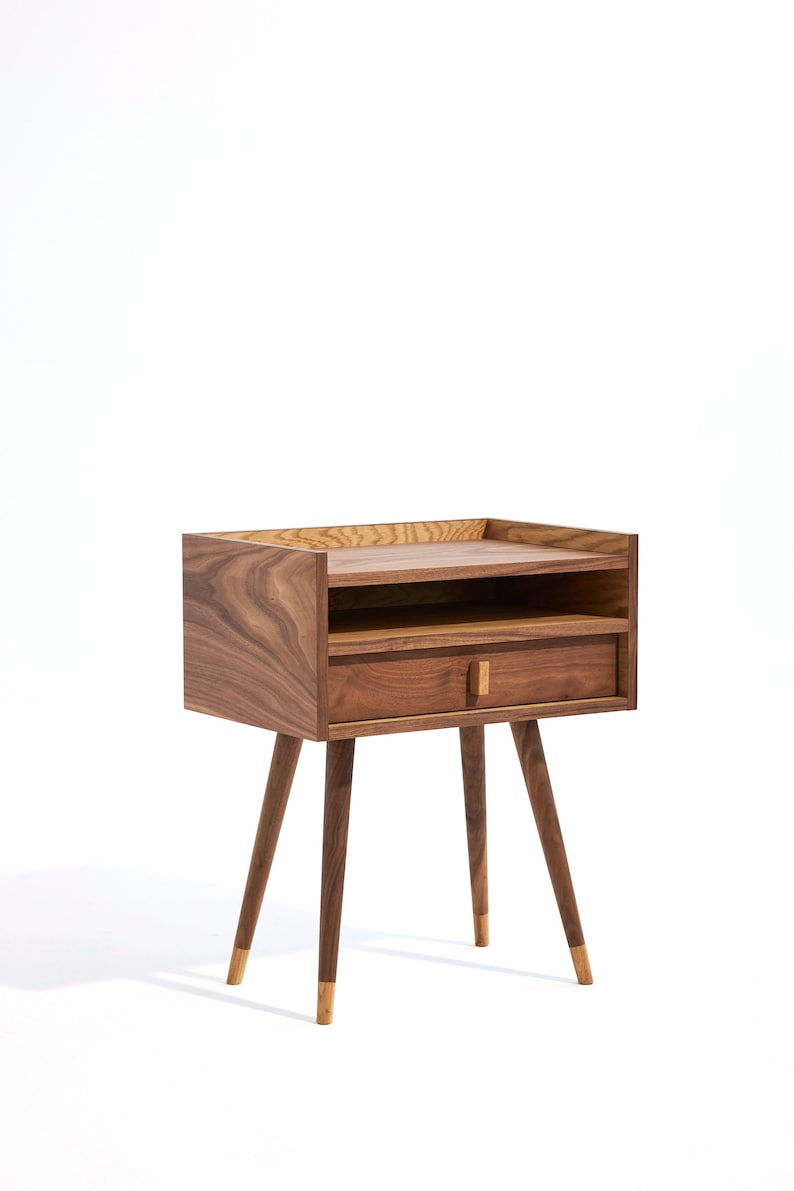 May include: A wooden nightstand with a drawer and a shelf. The nightstand has a dark brown finish and gold-tipped legs.