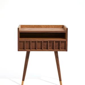 May include: A wooden nightstand with a shelf and a drawer. The nightstand has a dark brown finish and gold-tipped legs.