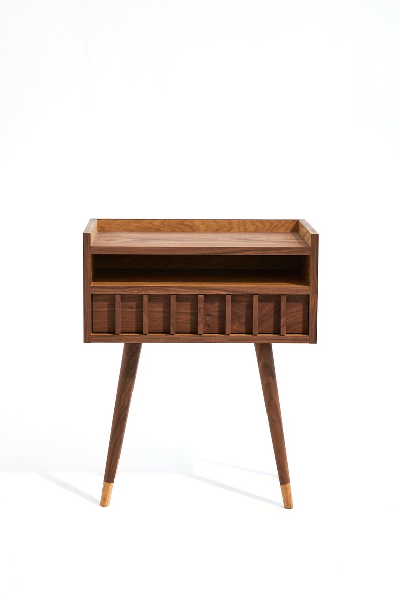 May include: A wooden nightstand with a shelf and a drawer. The nightstand has a dark brown finish and gold-tipped legs.