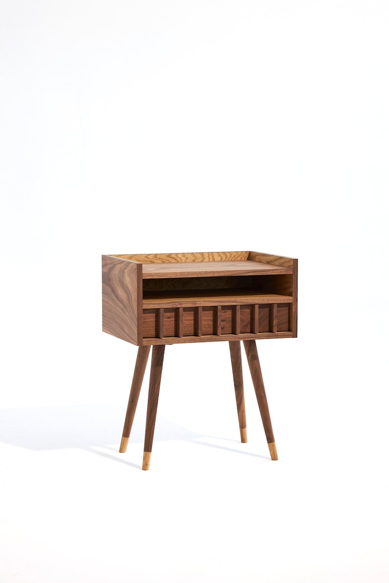 May include: A wooden bedside table with a shelf and a drawer. The table has a dark brown finish and gold-tipped legs.