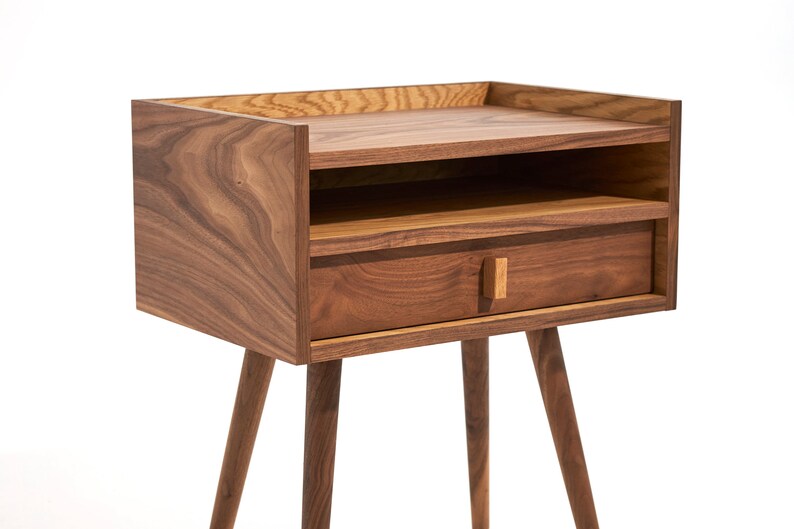 May include: A wooden nightstand with a drawer and a shelf. The nightstand has a dark brown finish and four legs.