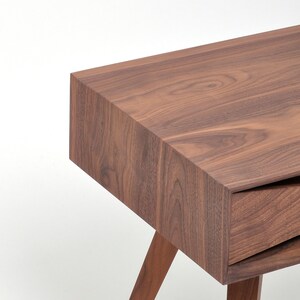 May include: A wooden end table with a drawer and angled legs. The table is made of dark brown wood with a natural wood grain.
