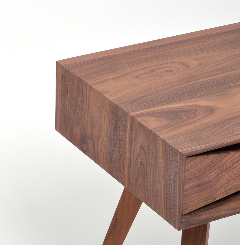 May include: A wooden end table with a drawer and angled legs. The table is made of dark brown wood with a natural wood grain.