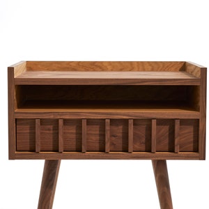 May include: A dark brown wooden nightstand with a shelf and a drawer. The drawer has a slatted front and the nightstand has tapered legs.
