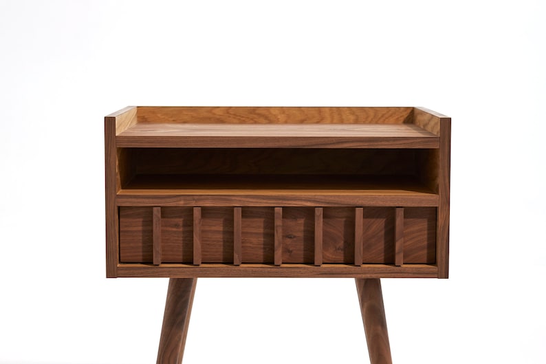 May include: A dark brown wooden nightstand with a shelf and a drawer. The drawer has a slatted front and the nightstand has tapered legs.