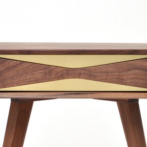 May include: A walnut wood nightstand with a single drawer featuring a brass inlay. The drawer has a unique, angled design. The nightstand has four legs.