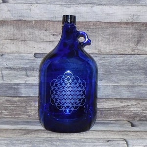 Könnte beinhalten: Eine kobaltblaue Glasflasche mit einem weißen, geätzten Design eines Lebensblumenmusters. Die Flasche hat einen schwarzen Deckel und einen Griff.