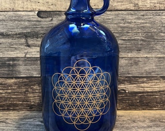 Blauwe glazen fles van 2 liter met handvat en Levensbloem G4-logo.