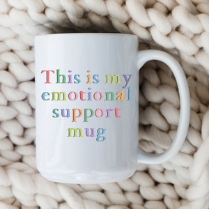 May include: White ceramic mug with the text "This is my emotional support mug" in rainbow colors.