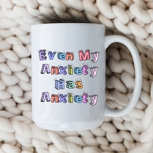 May include: White ceramic mug with a colorful, cartoon-style design that reads "Even My Anxiety Has Anxiety".