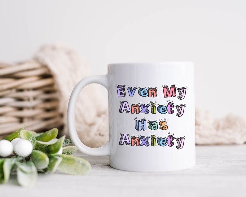 May include: White ceramic coffee mug with a colorful design that reads "Even My Anxiety Has Anxiety".