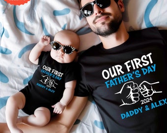 May include: A black t-shirt and a black bodysuit with the text "Our First Father's Day 2024 Daddy & Alex" in blue and white. The shirts feature a fist bump graphic.