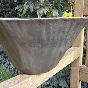 Könnte beinhalten: Ein großer, dunkelgrauer Keramiktopf mit einer breiten, ausgestellten Öffnung und einem gewellten Rand. Der Topf steht auf einer Holzoberfläche.