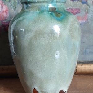 Op de afbeelding: Een handgemaakte keramische vaas met een glanzende afwerking. De vaas heeft een mix van groene en blauwe tinten, met een bruine basis en een druipglazuureffect. De vaas heeft een ronde vorm en een smalle hals, geschikt voor bloemstukken of als decoratie.