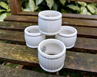 May include: Four white ceramic napkin rings with a ribbed design. The rings are stacked on top of each other.