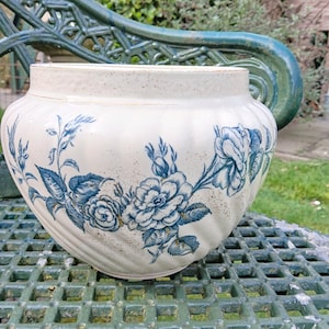 May include: A white ceramic planter with a blue and white floral design. The planter has a rounded shape and a slightly textured surface.