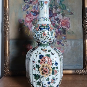 May include: A tall, ornate ceramic vase with a bulbous shape and a narrow neck. The vase is decorated with floral patterns in shades of orange, blue, green, and yellow against a white background. The vase is approximately 12 inches tall.