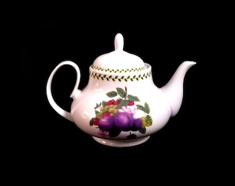 May include: White ceramic teapot with a lid, handle, and spout. The teapot is decorated with a colorful fruit design featuring purple plums, red raspberries, and green grapes. A green vine pattern adorns the rim of the lid.