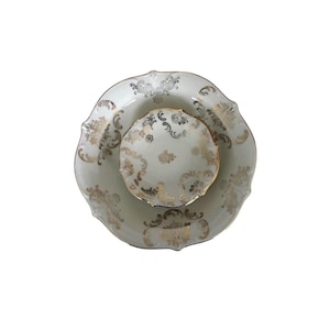 Può includere: Un set di tre piatti in porcellana bianca con disegni in filigrana dorata. Il set comprende un piatto grande con bordo smerlato, un piatto di medie dimensioni e un piccolo piatto rotondo. I dettagli dorati sono ornati e ricoprono i bordi e le superfici dei piatti.