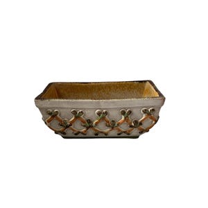 以下が含まれることがあります： クリーム色の外観と茶色の縁を持つ長方形のセラミックボウル。ボウルは、オレンジと緑の葉のようなデザインの繰り返し模様で装飾されています。内側は金色です。