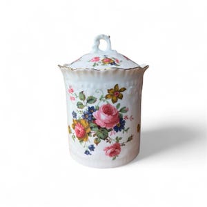 Könnte beinhalten: Ein weißes Keramikgefäß mit Deckel, verziert mit einem Blumenmuster mit rosa, gelben und blauen Rosen. Das Gefäß hat einen goldenen Rand und einen Schlaufengriff am Deckel. Das Design ist im klassischen Vintage-Stil gehalten.
