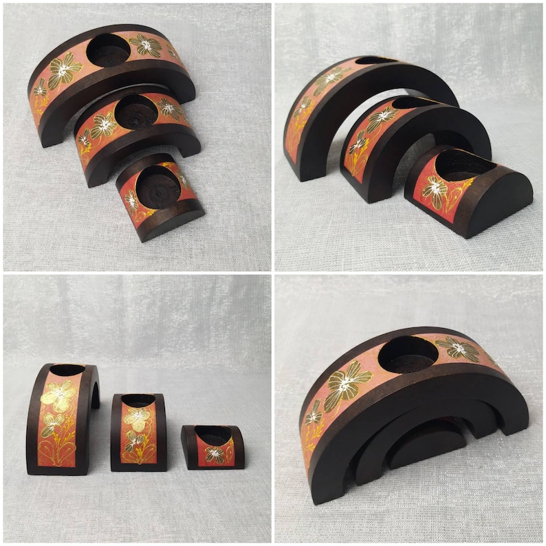 K&ouml;nnte beinhalten: Set aus drei unterschiedlich gro&szlig;en Kerzenhaltern aus Holz. Die dunkelbraunen Halter haben ein geschwungenes Design mit einem rosa Band mit goldenen und wei&szlig;en Blumenmustern. Jeder hat eine kreisf&ouml;rmige &Ouml;ffnung f&uuml;r Kerzen.