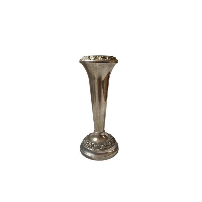 May include: A silver-colored bud vase with a flared top and a decorative base. The vase has a slender, conical shape and is likely made of metal. The base and top rim feature ornate detailing, adding to its vintage appeal.