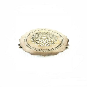 Op de afbeelding: Een zilverkleurige, ronde onderzetter met een decoratief bloemmotief in het midden. De onderzetter heeft een geschulpte rand en een gedetailleerd opengewerkt ontwerp. Dit keukenaccessoire is ontworpen om oppervlakken te beschermen tegen hete gerechten.