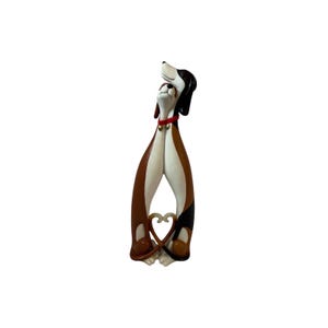 May include: A decorative dog ornament in brown, white, and black. The dog is depicted in a stylized pose, looking upwards. It features a red collar and a gold heart-shaped base. The ornament is made from a glossy material.