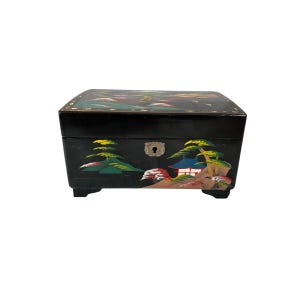 May include: Black wooden jewelry box with hand-painted landscape scenes. The box features a keyhole and is adorned with colorful trees, mountains, and a traditional building. The box sits on four small feet.