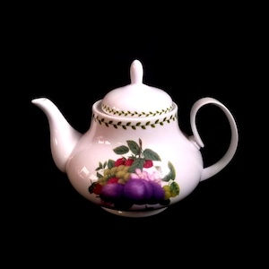 Puede incluir: Tetera de cerámica blanca con tapa, con un diseño de frutas de ciruelas moradas, frambuesas rojas y uvas verdes. El borde y la tapa tienen un patrón de vid verde. La tetera tiene un asa y un pico curvos.