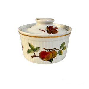 Puede incluir: Cazuela de cerámica blanca con tapa, con borde dorado y un diseño decorativo de manzanas y hojas. El plato tiene una textura acanalada y un pequeño pomo en la tapa. Una adición encantadora a cualquier cocina.