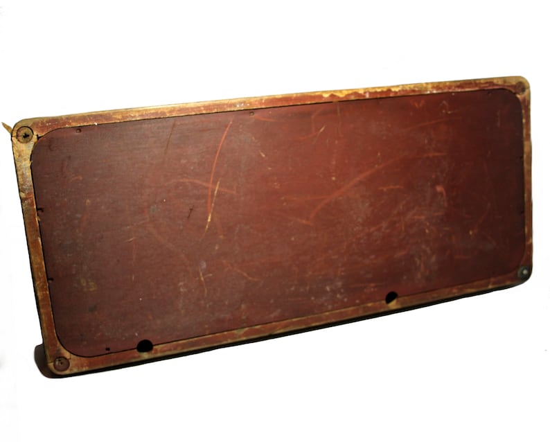 May include: Rectangular, vintage-style wooden sign with a distressed, reddish-brown surface. The sign has a gold-colored metal frame and visible screw details. The wood shows signs of wear and tear.