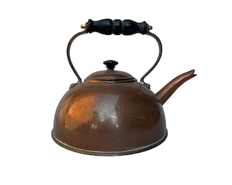 May include: A copper-colored kettle with a black wooden handle and spout. The kettle has a rounded body, a lid with a black knob, and a curved handle. The handle is attached to the kettle with metal brackets. The spout is curved and pointed.