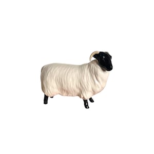 May include: A ceramic sheep figurine with a white body and black head, legs, and hooves. The sheep has curved horns and a fluffy wool texture. The figurine is standing on a white surface.