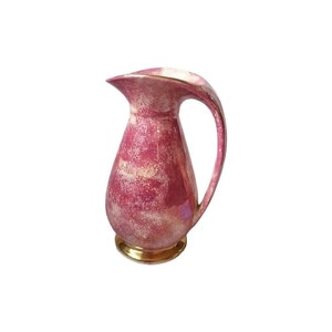 May include: A vintage pink and gold jug with a curved handle and spout. The jug has a speckled design with gold accents on the base and rim. The jug is a decorative item.
