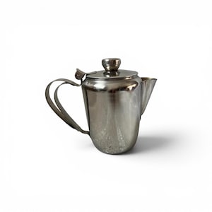 May include: A polished stainless steel teapot with a rounded body, a curved handle, a hinged lid featuring a small knob, and a short, angled spout. The metallic surface reflects light, showing a smooth, reflective finish on the exterior.