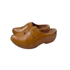 May include: A pair of wooden clogs, painted with decorative details. The clogs are a light brown color, with red and black accents. The clogs are a traditional style, with a rounded toe and a curved sole. The clogs are likely handmade.