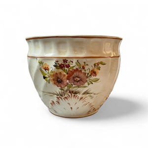 May include: Cream ceramic plant pot with a hand-painted floral design. The flowers are in shades of brown, orange, and yellow, with green leaves. The rim and base have a brown trim. The pot has a slightly ruffled edge.