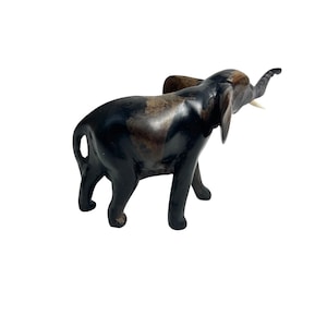 May include: A small, dark brown wooden elephant figurine with a raised trunk and ivory-coloured tusks. The elephant has large ears and is standing on four legs. The figurine has a smooth, polished finish against a white background.