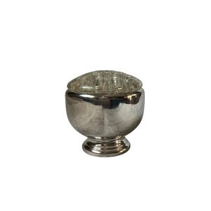 May include: A silver-coloured, footed bowl with a clear glass flower frog lid. The bowl has a rounded body and a pedestal base. The glass lid is round and has multiple holes for arranging flowers. Likely vintage.