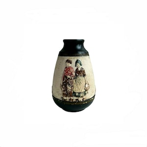 May include: A vintage ceramic vase with a black top and base, featuring a cream-colored body. The body is decorated with a relief of two figures in traditional clothing, each carrying a basket. The vase has a bulbous shape.