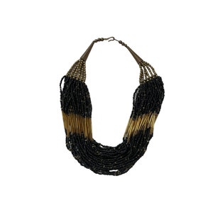 Pode incluir: Colar de várias voltas com contas pretas e contas cilíndricas douradas. O colar tem um fecho de gancho e peças finais decorativas em forma de cone metálico. Uma peça de joalharia marcante.